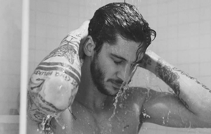 Head and torso of a dark-haired man washing his hair in the shower